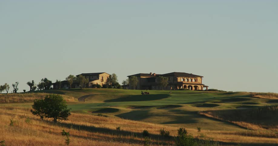 Golfer moves over course with club houses in the background