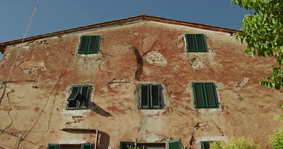 A cracked and damaged exterior of a stucco building under a bright blue sky