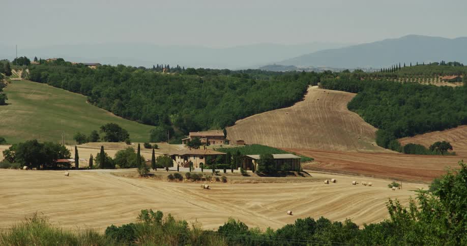 Small buildings in the middle of a farm in the gentle slopes of a hill next to the mountains
