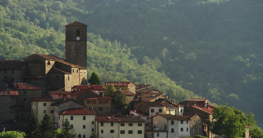 Red roofed village with clock tower stands on forested slope near foggy valley
