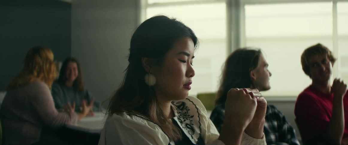 A young woman talks to her classmates before looking away disappointedly