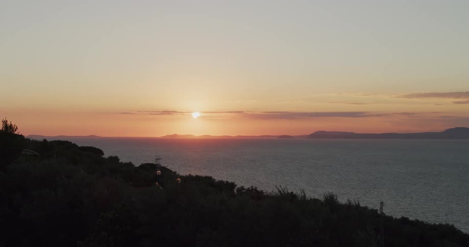A machine moves on the hillside overlooking the water as the sun sets in a hazy sky