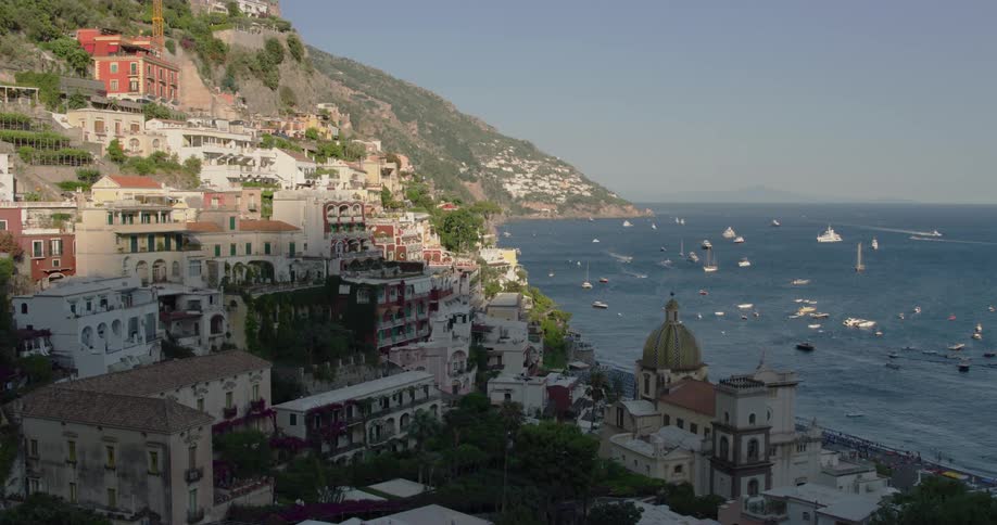 A village on a mountain is on the coast of a sea filled with boats
