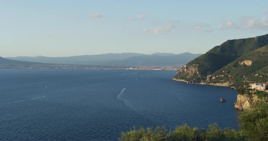 Boat moving over the calm blue ocean water close to a coastal town at daytime