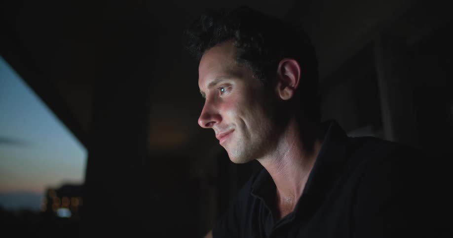 Man sitting on a dark room at home working on a computer at evening