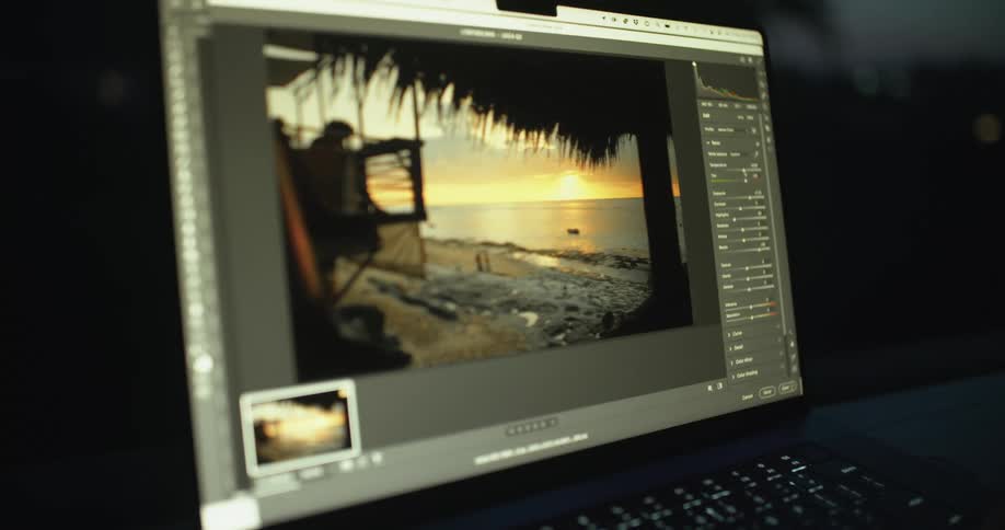 Someone is sitting at a table in a dark room adjusting photographs on a laptop computer