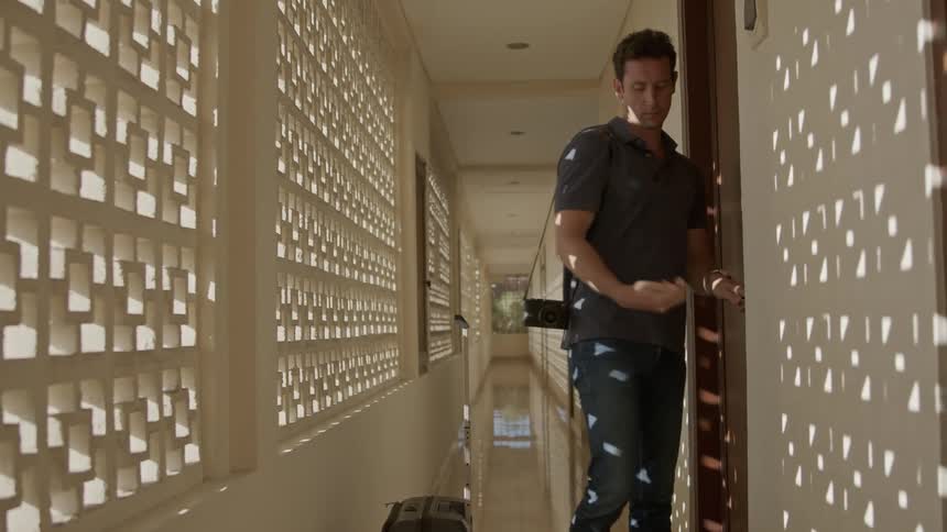 Man leaving the room closing the door and carrying his suitcase down a hallway