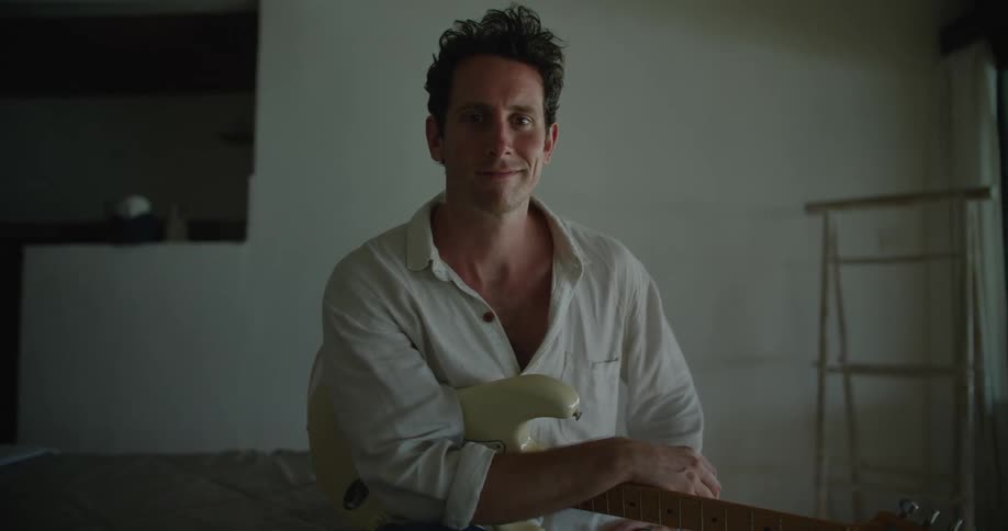 A man is sitting and holding a guitar