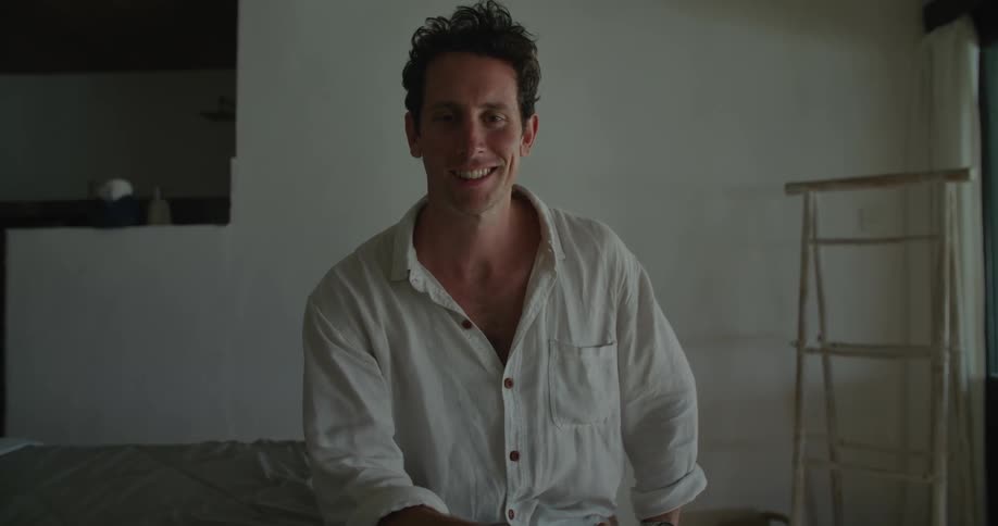 A man is sitting down and he turns his head to look forward and smiles