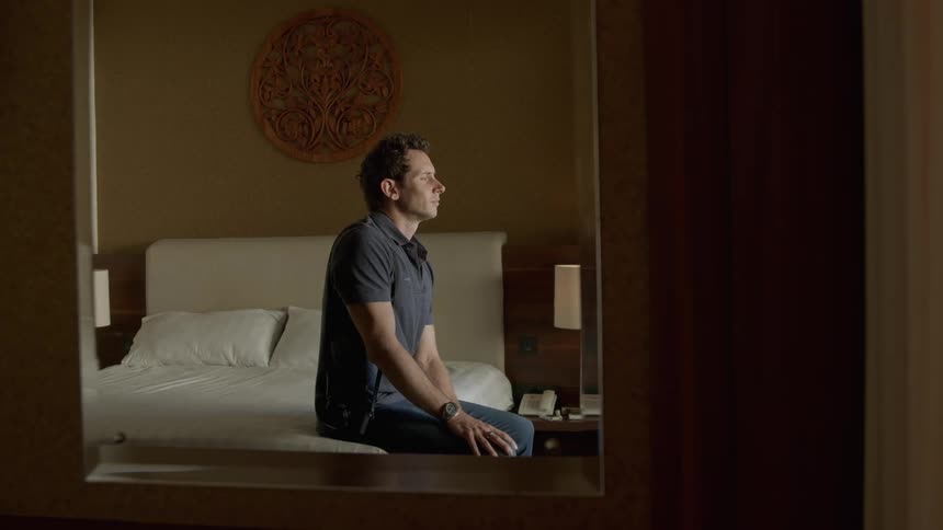 Mirror reflection of a thoughtful man sitting on hotel bed looking at his smartphone and then lying down