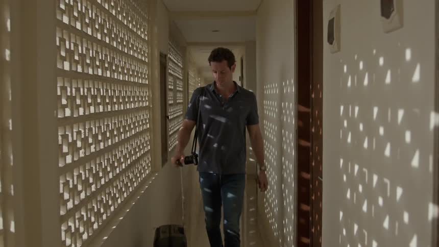 Photographer carrying luggage through a narrow hotel hallway opens the door to enter his room