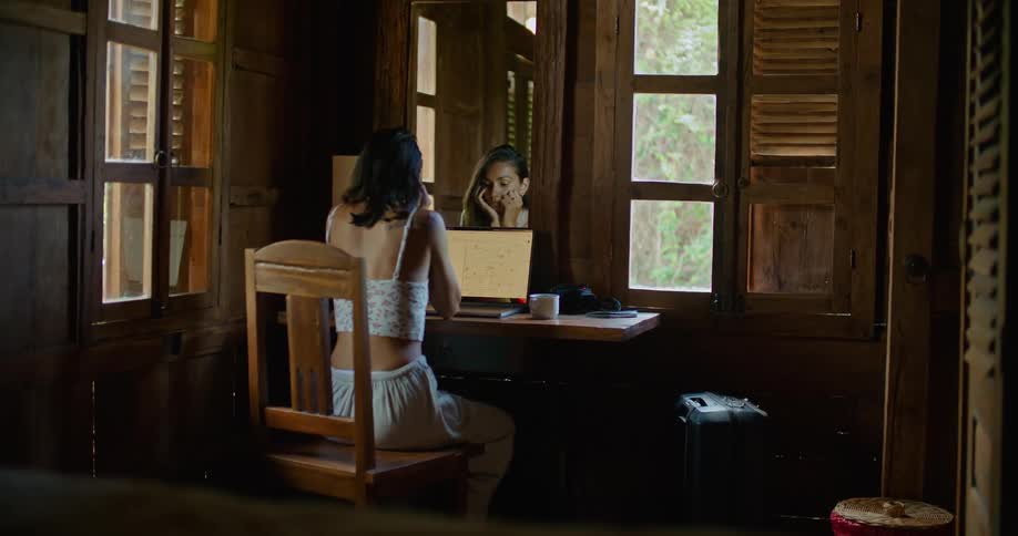 Young woman sitting at a desk at home typing on a laptop in front of a mirror