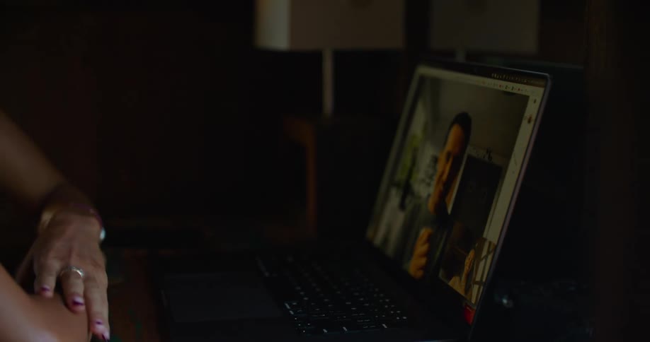 Woman with with straight hair earrings printed halter blouse and tattoo makes video call on laptop smiling
