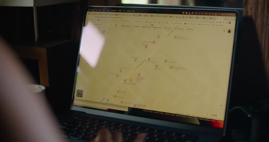 Camera pans from a womans reflection to what she is viewing on her laptop