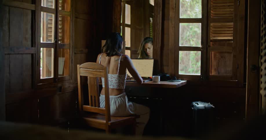 Young woman sitting at the desk in front of a mirror using her laptop