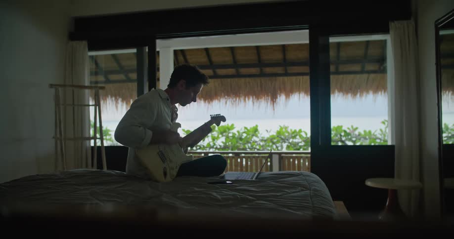 Man plays guitar while looking at music on his laptop