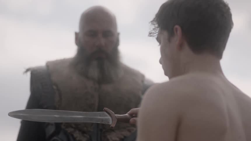 A large man hands a younger man a large knife