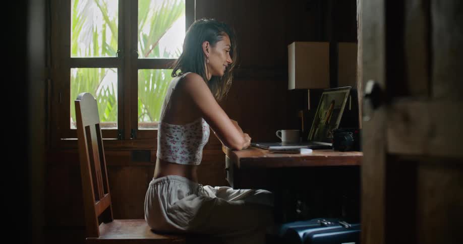 Woman with straight hair earrings printed halter blouse and tattoo makes video call on laptop