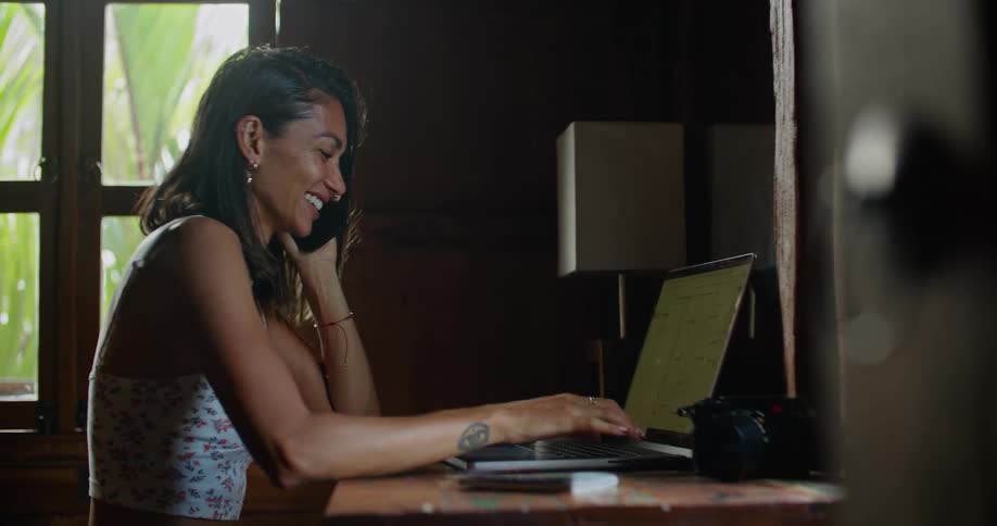 A woman is sitting down in front of a laptop computer and talking on the phone