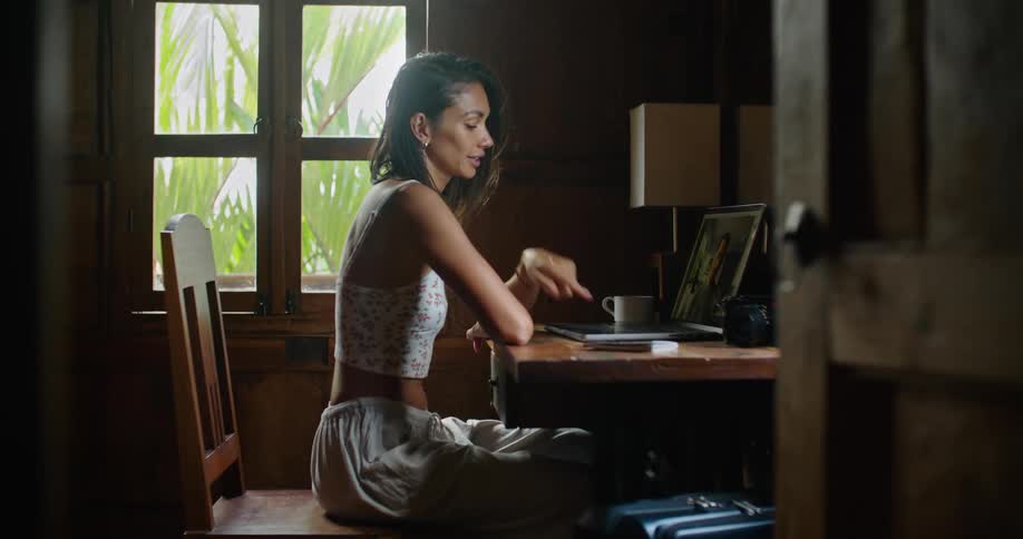 Young happy woman sitting at a desk at home talks on a video call on a laptop