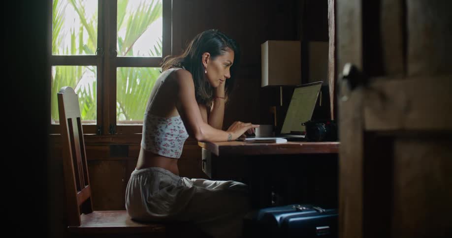 Woman sitting at the wooden desk next to the window typing on her laptop