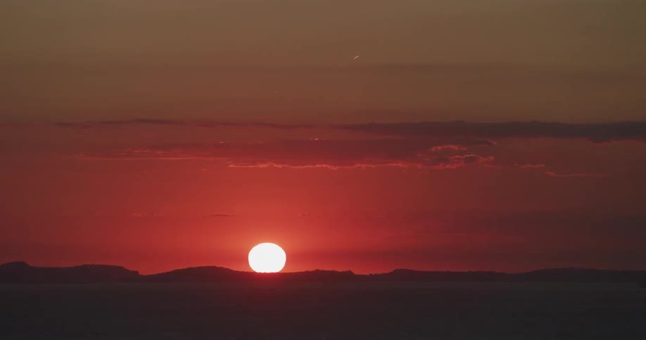 The sun sets behind mountains in a deep red sky