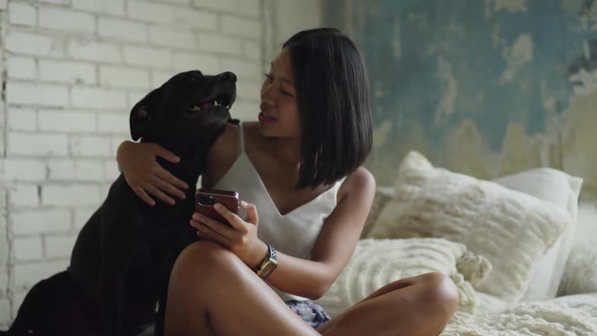 A woman smiling and petting her dog while sitting in bed