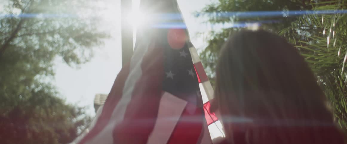 Daughter watches as father hangs flag on flagpole on sunny day