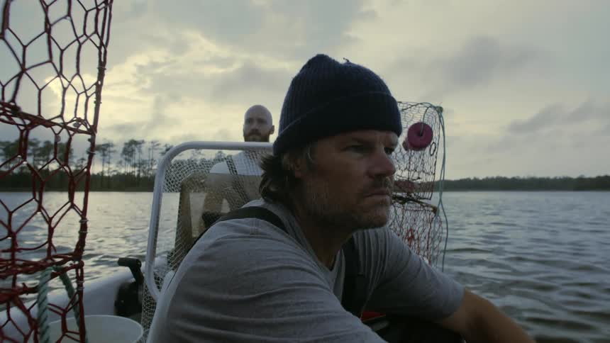 A man sitting on a fishing boat next to traps while another drives away from land