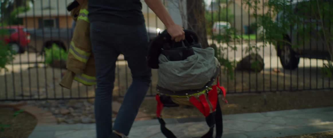 A firefighter carries his uniform and a backpack while walking to his vehicle