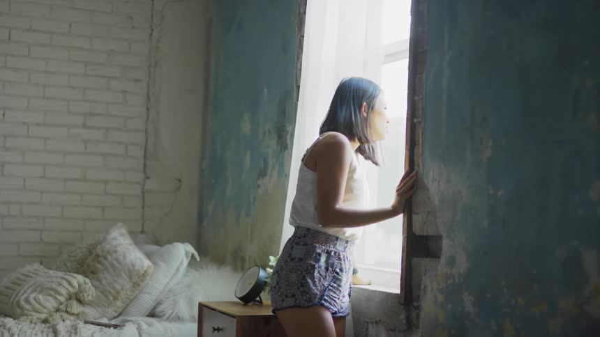 A woman walks to her bedroom window and looks out