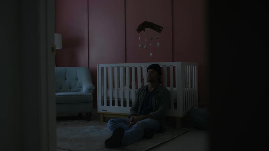 A man falls asleep while leaning against his babys crib