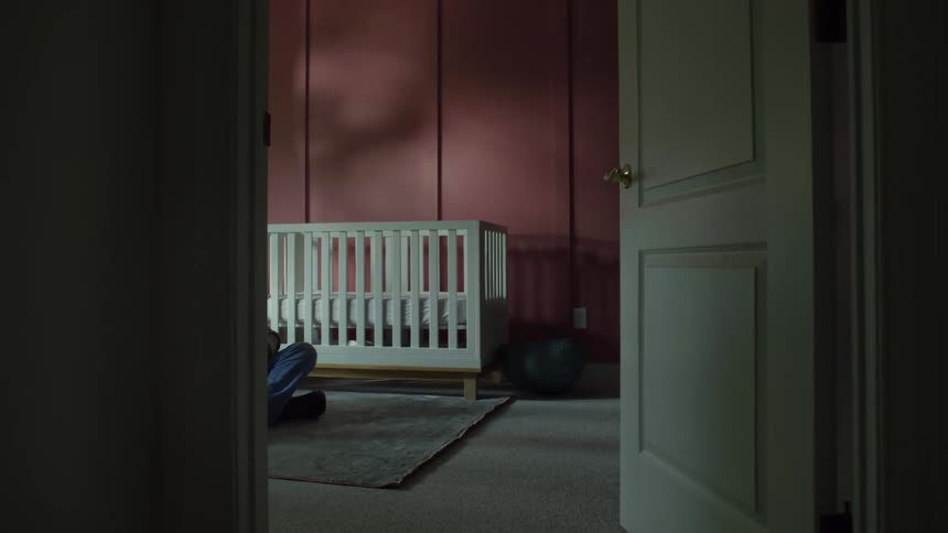 A man rocks a baby in his arms while sitting on the floor of bedroom during the day