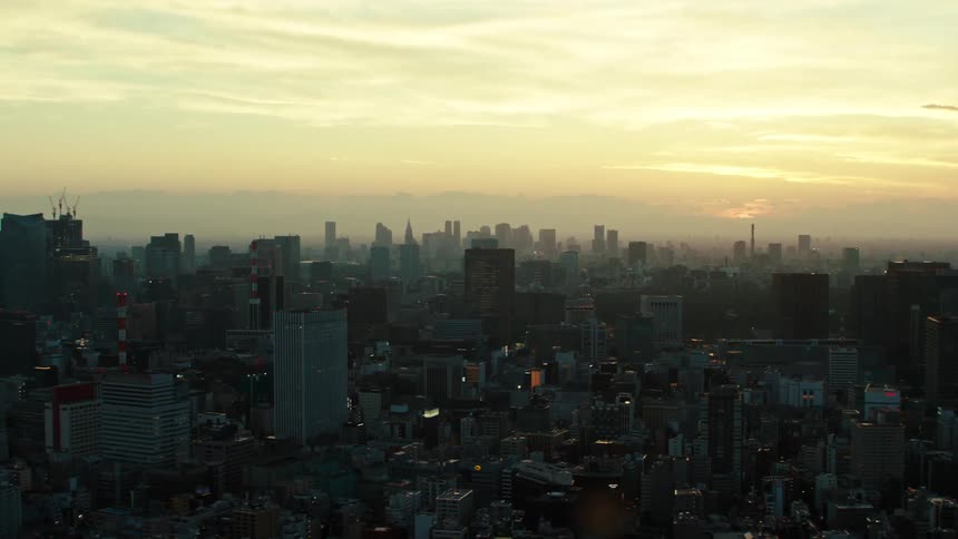 Towers and skyscrapers stand tall over a big city as the sun shines through the clouds in a hazy sky
