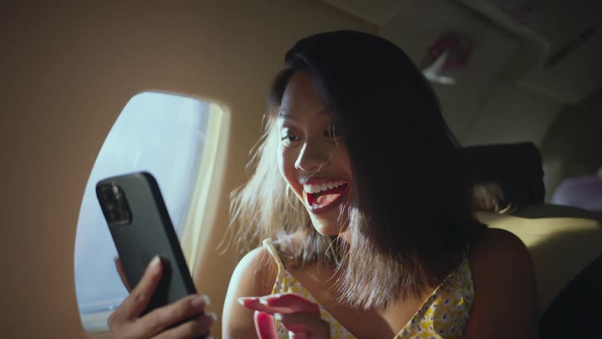 A woman smiling and holding a smartphone while traveling on an airplane