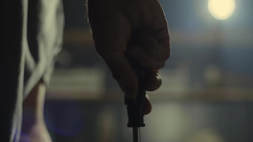 Silhouette of the hand of a man turning a scrwedriver on a dimly lit room