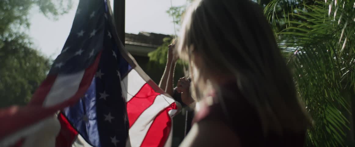 Blonde girl and man hang american flag on flag pole