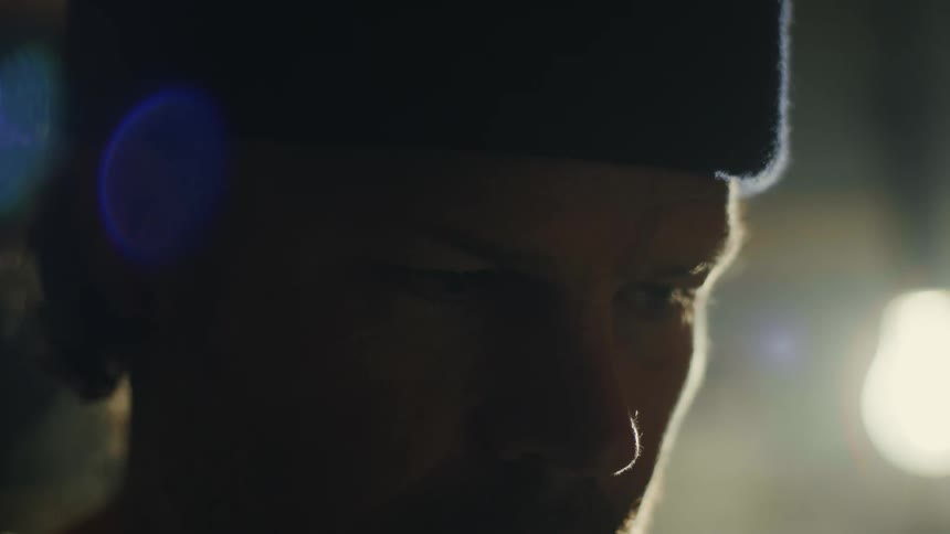 A man wearing a hat looking down pauses looks up then continues his work