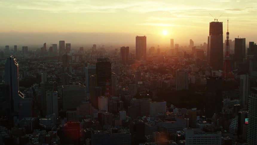Towers and skyscrapers stand tall over a big city as the sun is on the horizon in a hazy sky