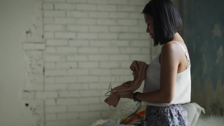 A woman is standing in a room folding clothes and putting them into a suitcase