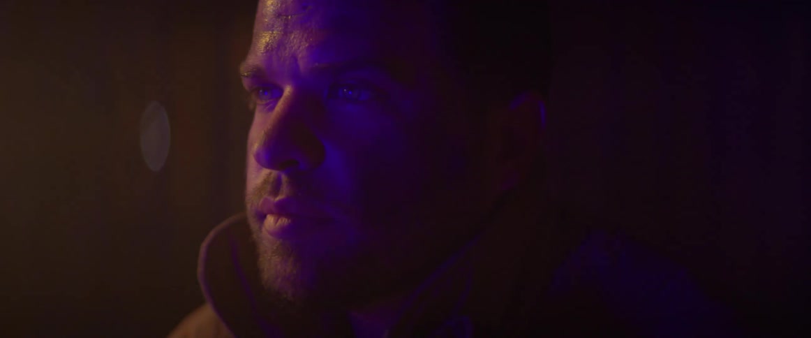 Close up of the face of a man wearing a thick jacket under flashing red and blue lights