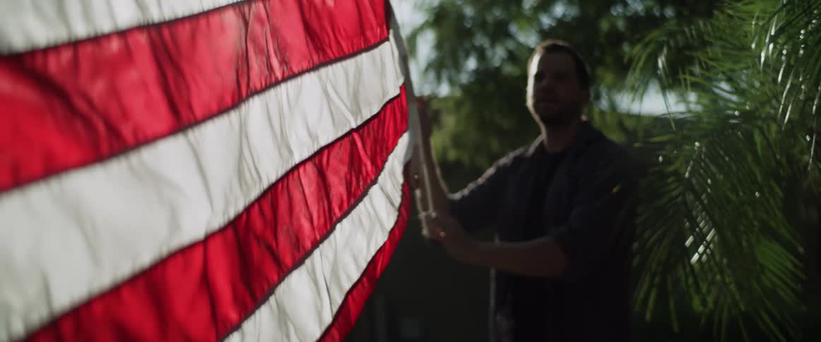 A man holds the rope of a flag attached to flagpole outdoors during the day