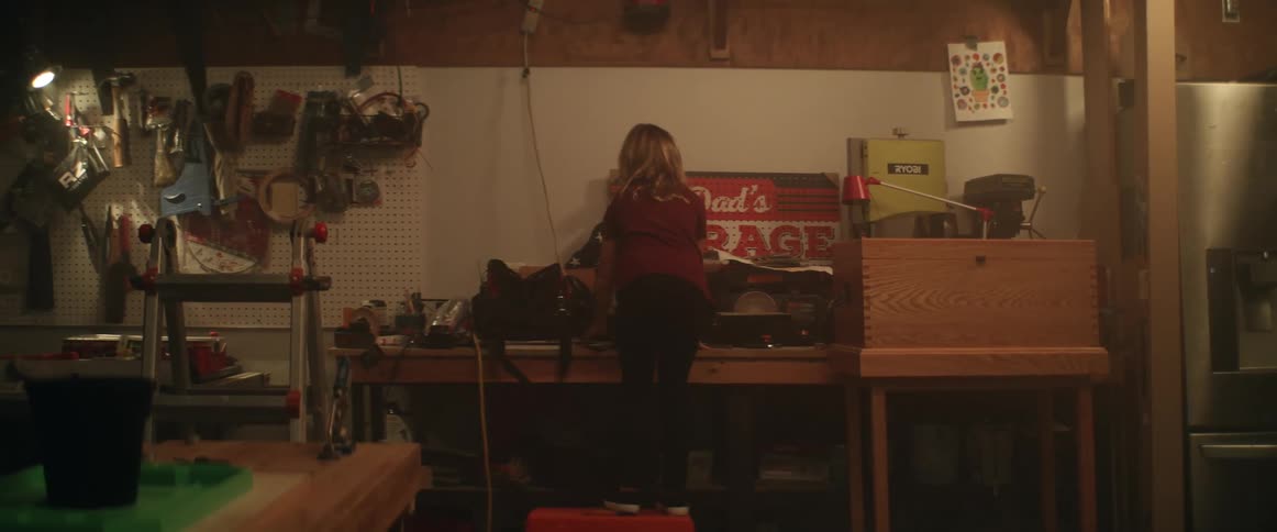 A little girl is in the garage climbing up on a table to get something and she finds what she is looking for and leaves