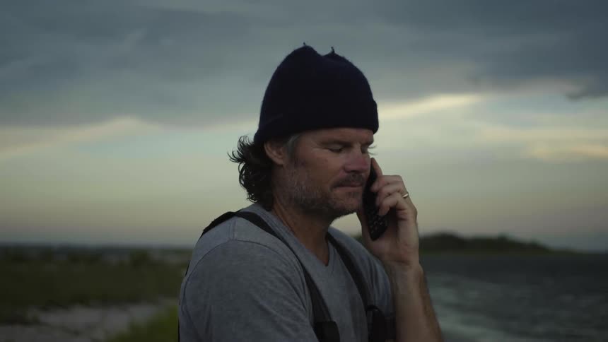 A man talks and hangs up his cell phone on the shore