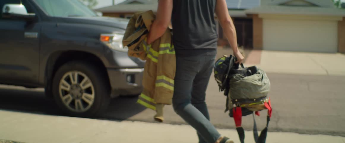 A firefighter carries his equipment on the sidewalk