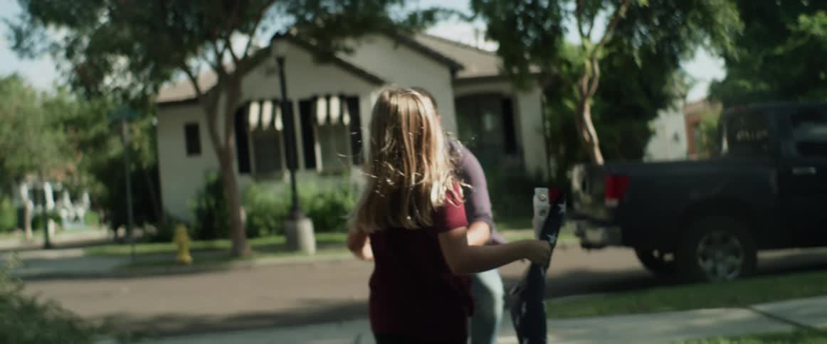 Blonde girl runs to greet man with a hug while carrying an american flag