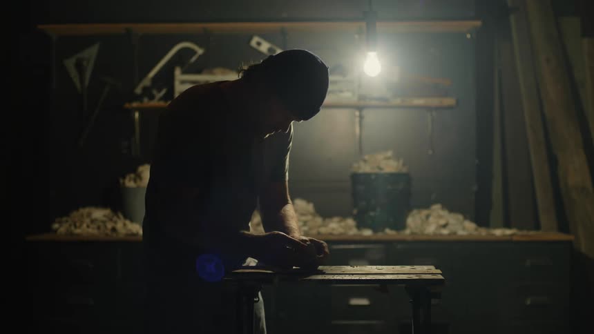 Silhouette of a sculptor working on a handmade piece over a small workbench in a dimly lit workshop