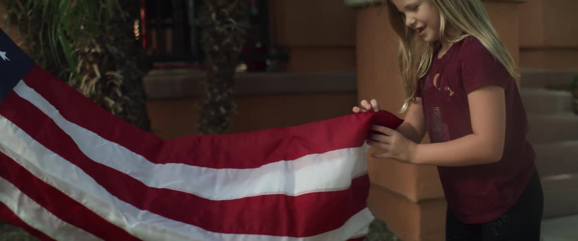 A girl helps her father unfurl an american flag