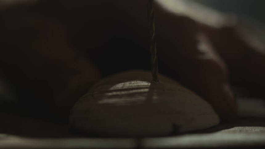 Extreme close up of a man drilling a seashell to make a hanging ornament on a dimly lit room