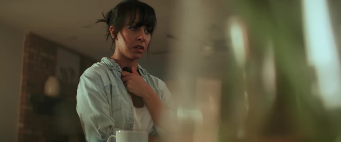 A woman holds a phone against her ear and then anxiously moves it down and holds it against her chest before talking again